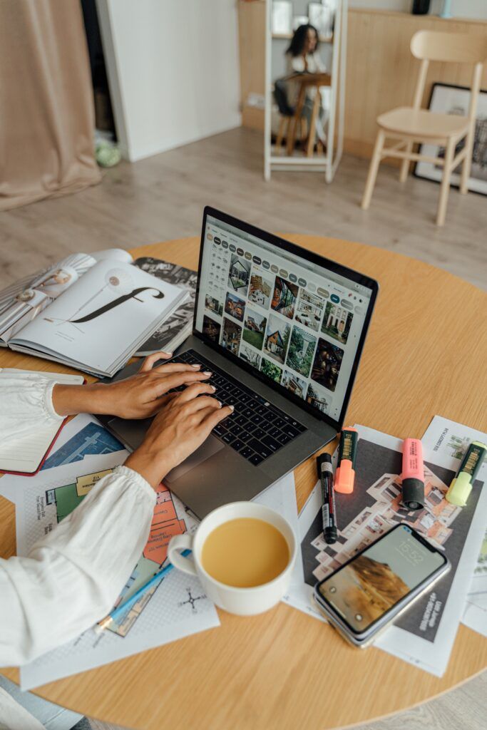 Hands showing typing on a desk with magazines highlighters, pencil, printed papers, and cup of coffee using laptop